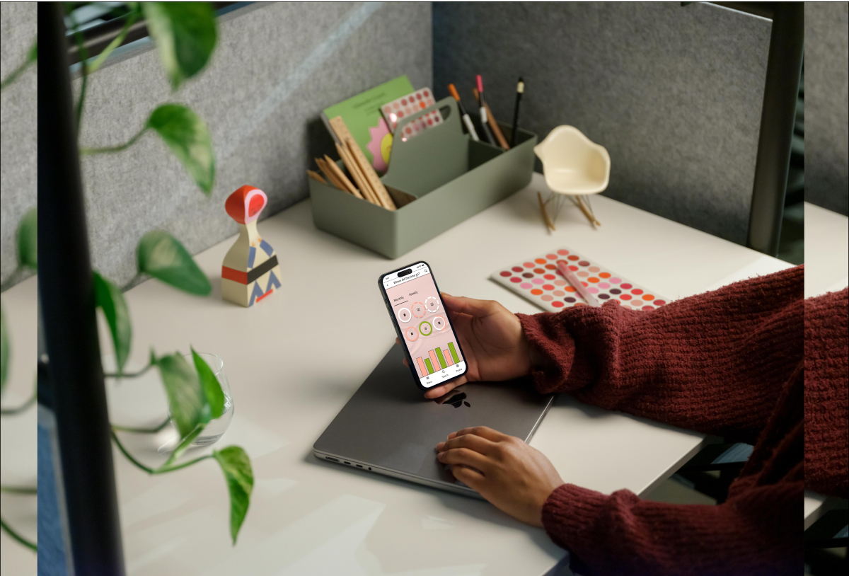 A person sitting at a desk, holds a phone with the habits app screen of Procrastigreat open.